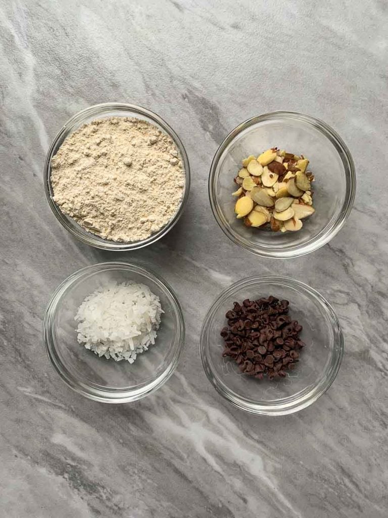 This is a picture of the ingredients for the almond joy pancakes. There are four small bowls, one with pancake mix, one with almonds, one with coconut, and one with chocolate chips.