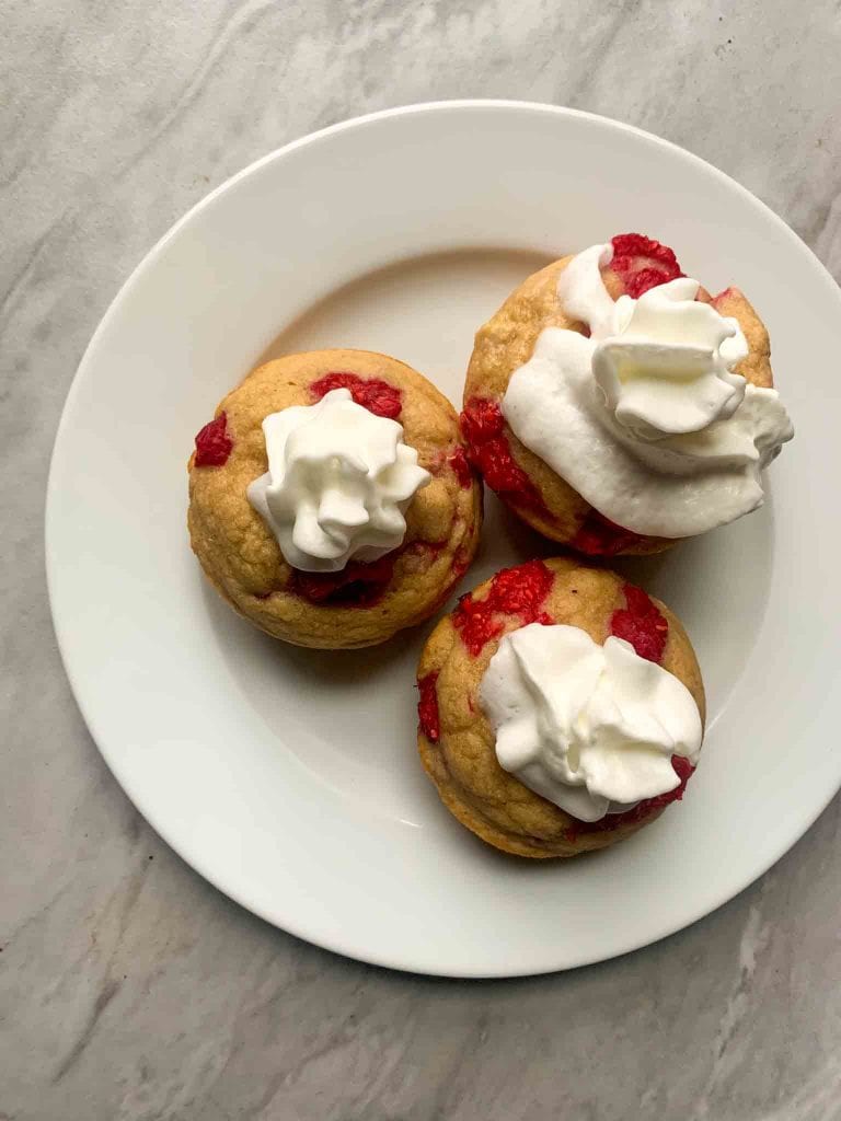 This is a small plate of pancake bites with raspberries topped with whipped cream.