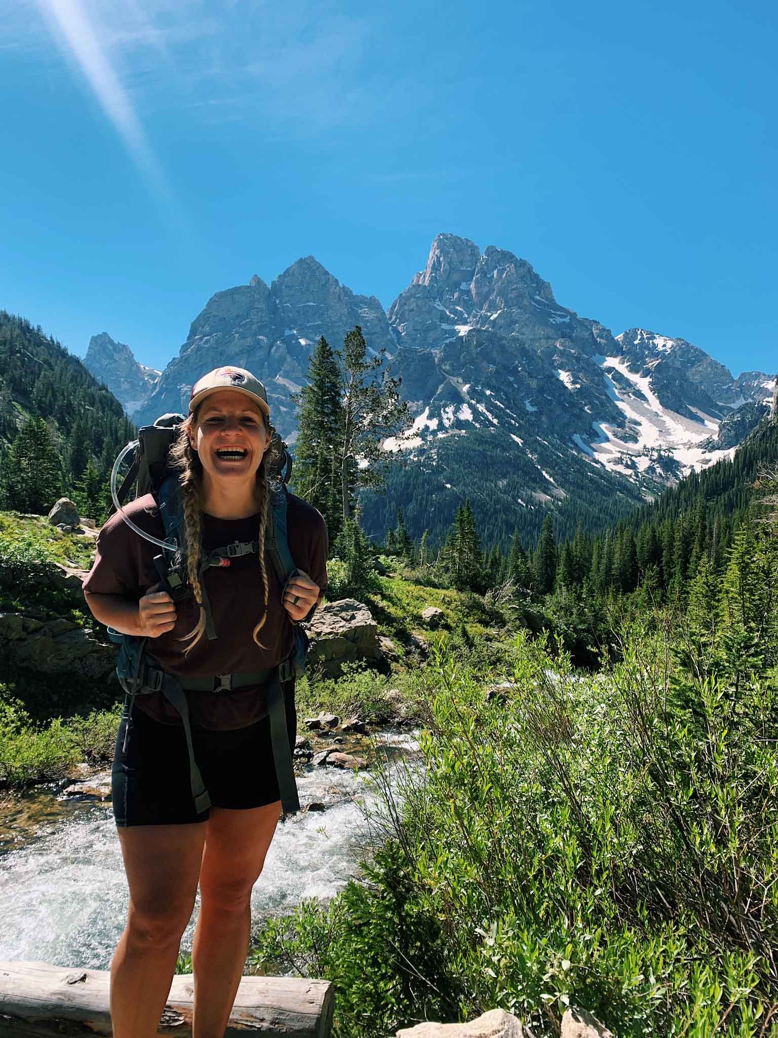 This is a girl hiking in grand teton national park. She is wearing a maroon shirt and standing in front of mountains.