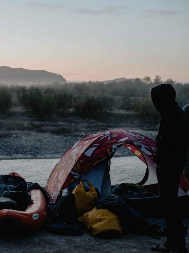 This is a picture of a tent with an open door. There's camping gear around and the tent is in front of a river with fog around it.