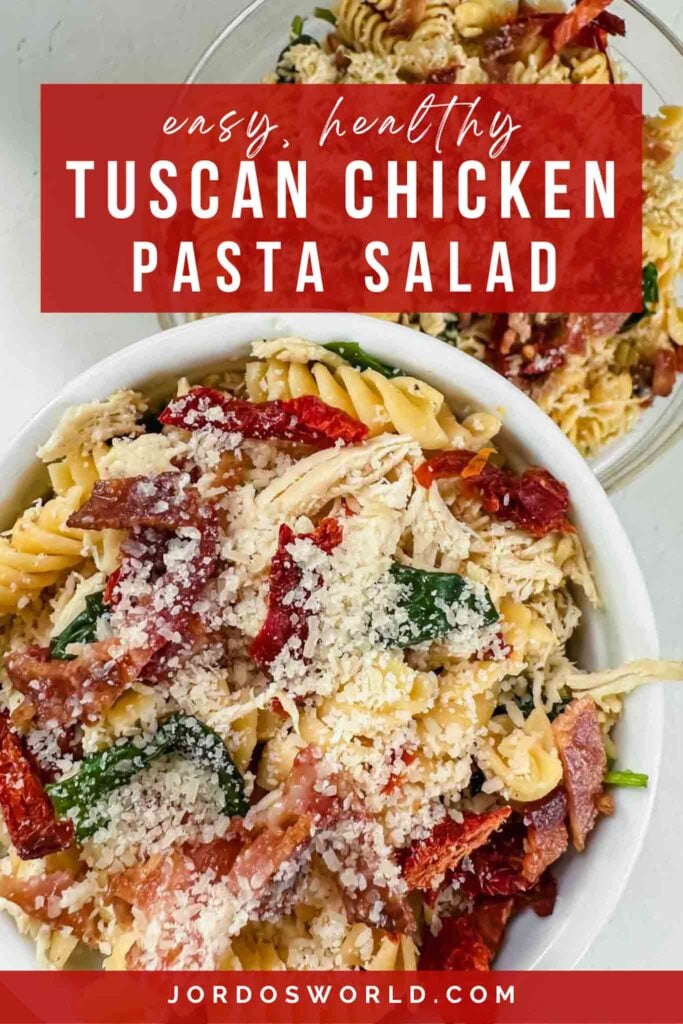 This is a pinterest pin for tuscan chicken pasta salad. There is a clear glass bowl filled with pasta, shredded chicken, spinach, dried tomatoes, bacon, and cheese. Everything is mixed together and the title of the recipe is above the image.