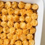 This is a picture of cheeseburger tater tot casserole. There is a large white casserole dish filled with the casserole. There's a layer of tater tots topped with melted shredded cheese.