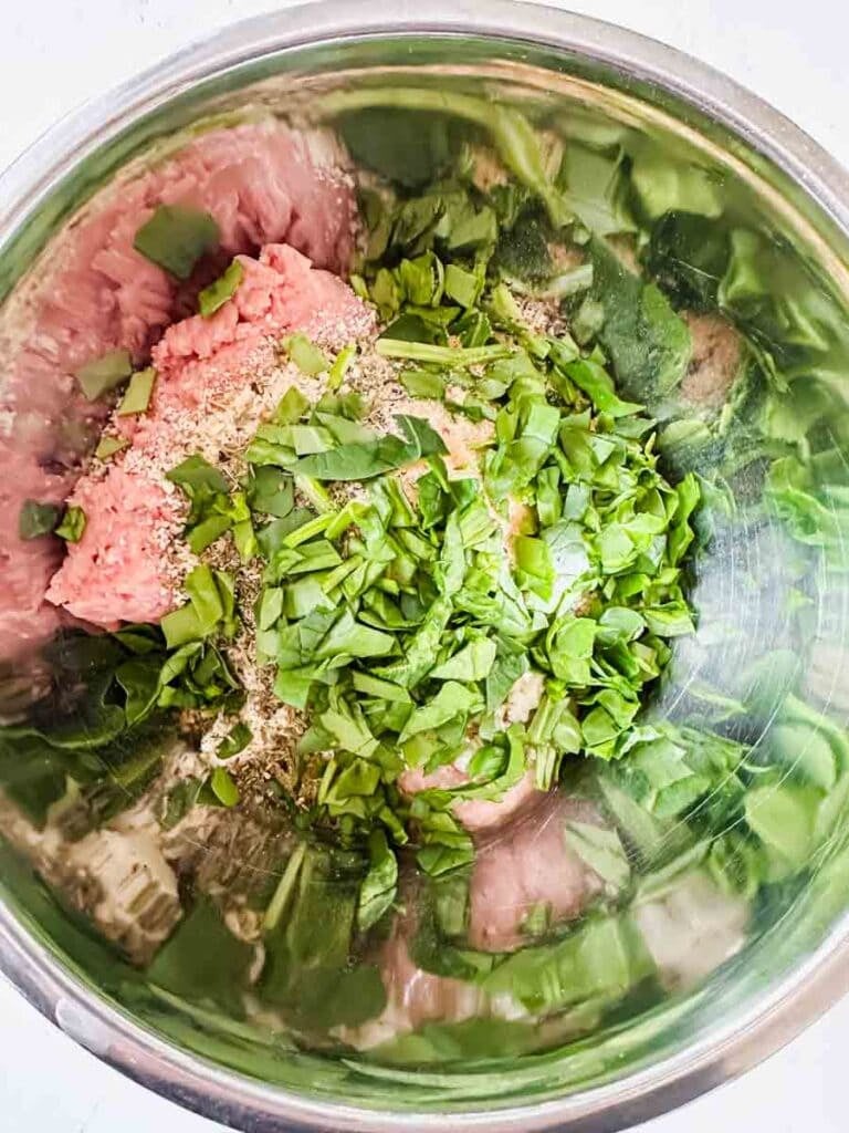 This is a bowl filled the ingredients for greek turkey meatballs. There's ground turkey, chopped spinach, parsley, seasoning, and breadcrumbs.