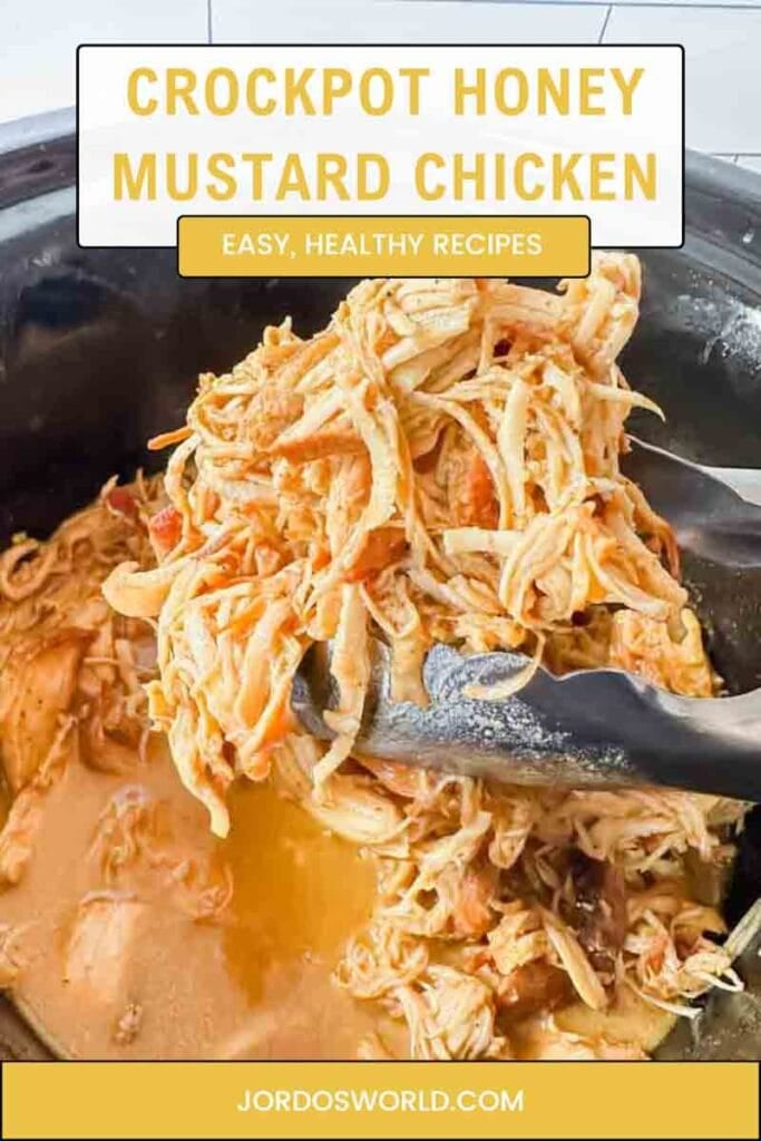 This is a pinterest pin of honey mustard chicken. This is a picture of crockpot honey mustard chicken. There is large black crockpot filled with shredded chicken in a orange honey mustard sauce. There's silver tongs holding shredded chicken.
