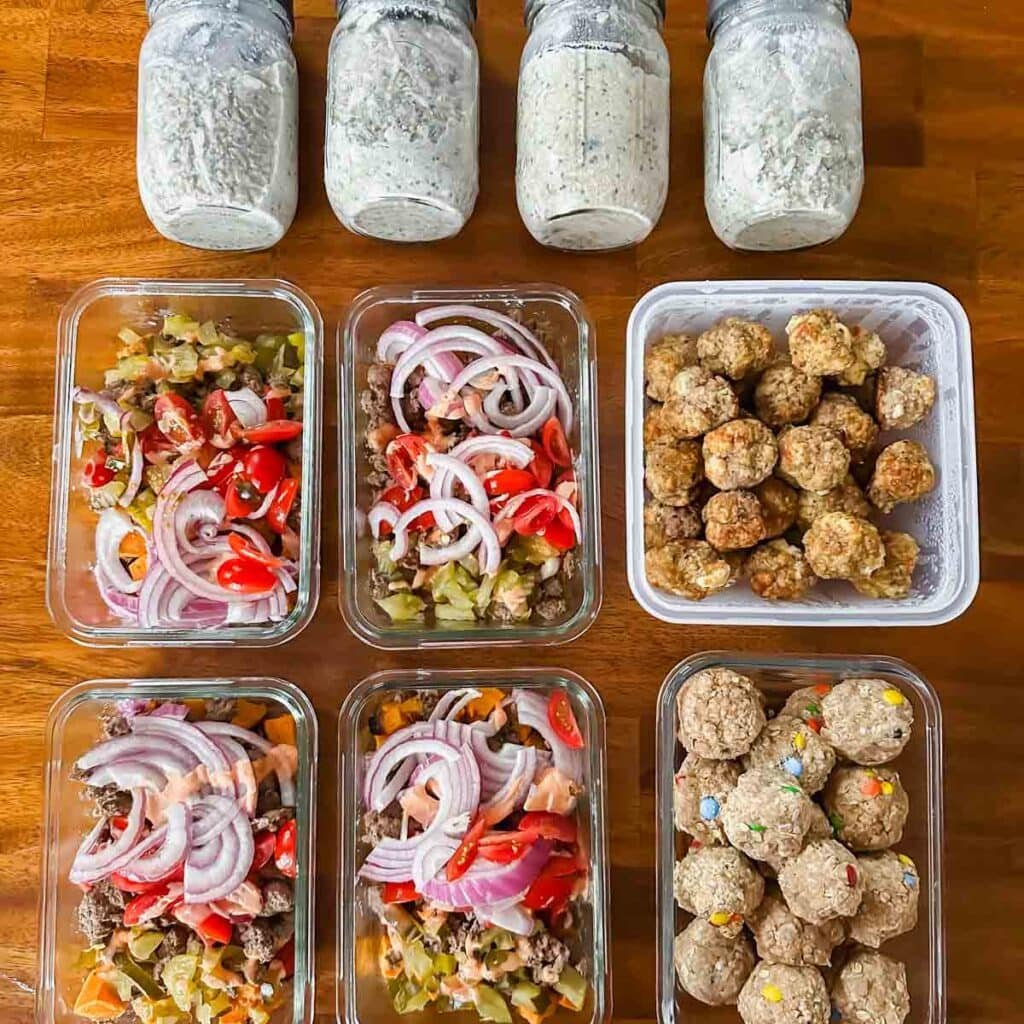 This is a picture of weekly meal plan 43. There are containers of all the prepped food organized on the table. There's mason jars of oats, burger bowls, meatballs, and protein balls.