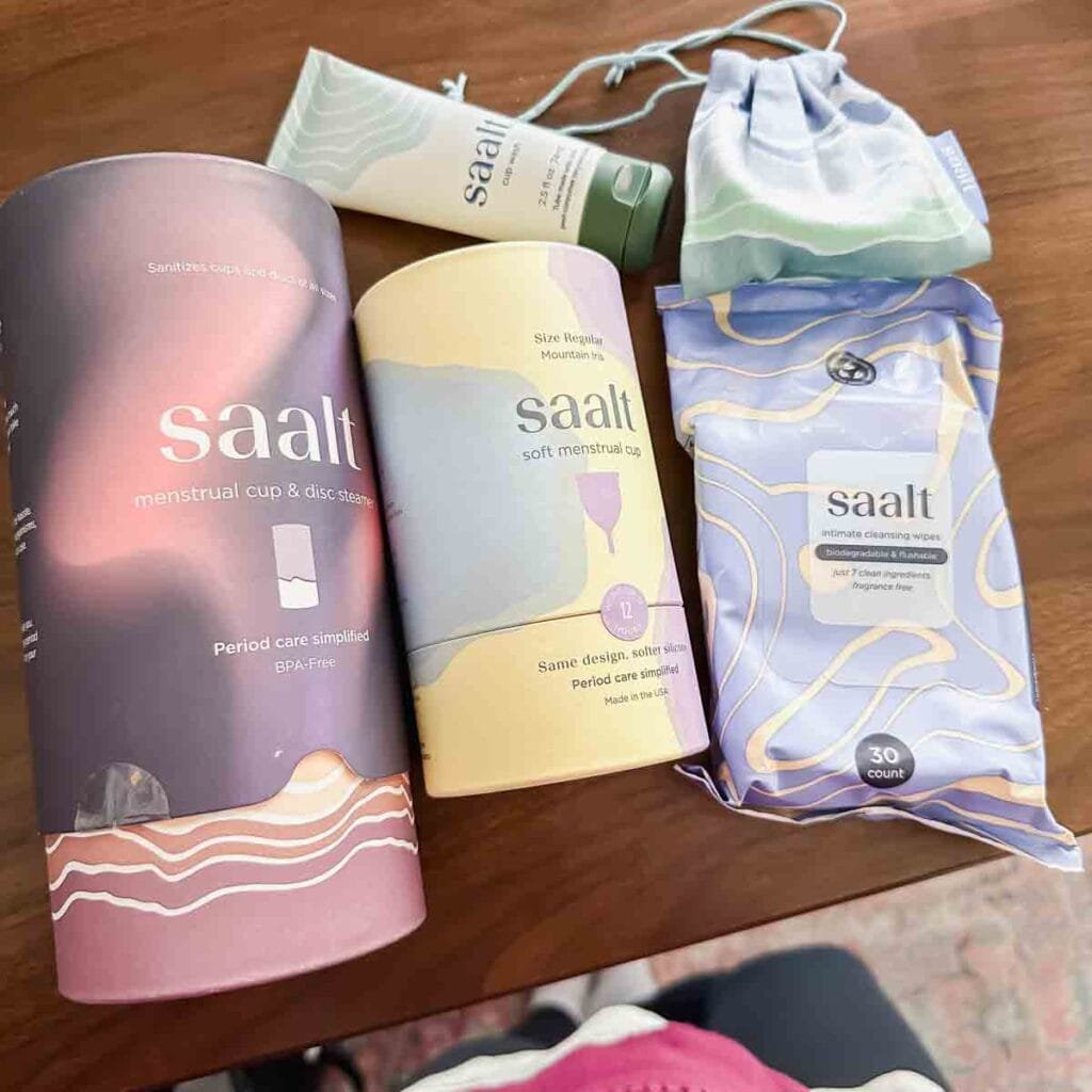 This is a picture of Saalt reusable period products. There's a cup, disc, wipes, and cleaner all together on a table.