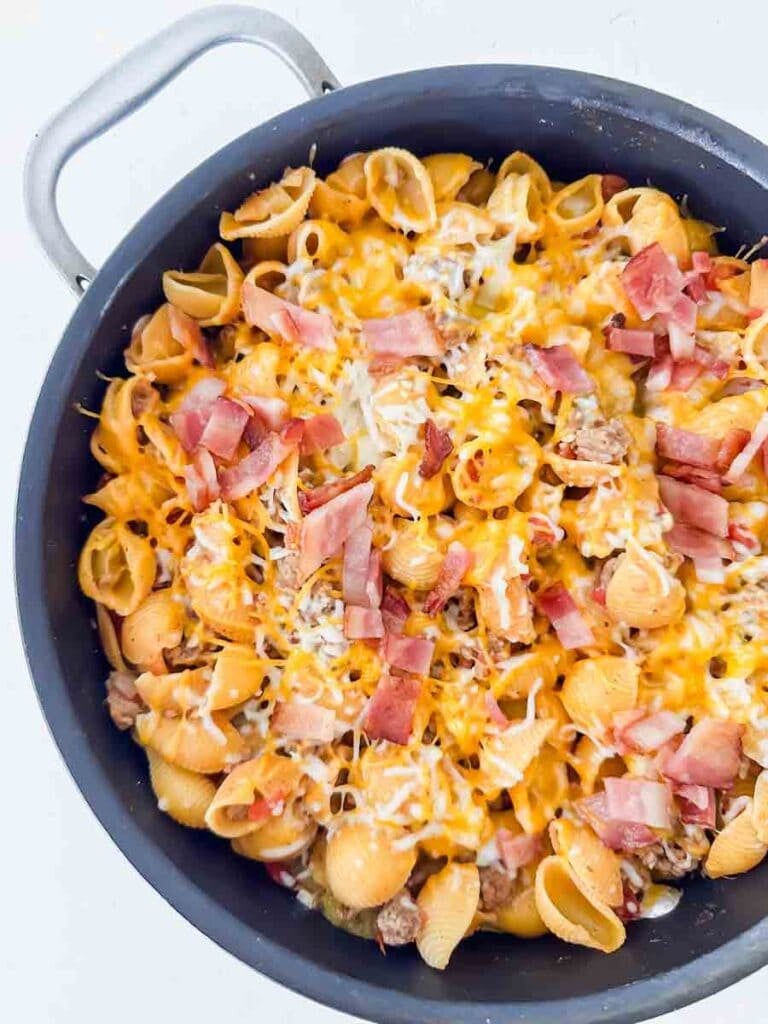 Cheesy pasta with bacon and cheese in a large black skillet. This is bacon cheeseburger skillet.