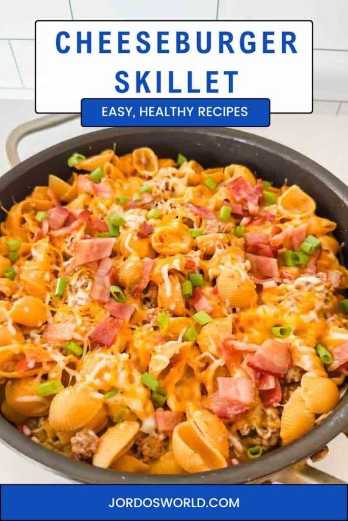 Cheesy pasta with bacon, green onions, and cheese in a large black skillet. This is bacon cheeseburger skillet.