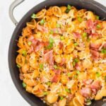 Cheesy pasta with bacon, green onions, and cheese in a large black skillet. This is bacon cheeseburger skillet.
