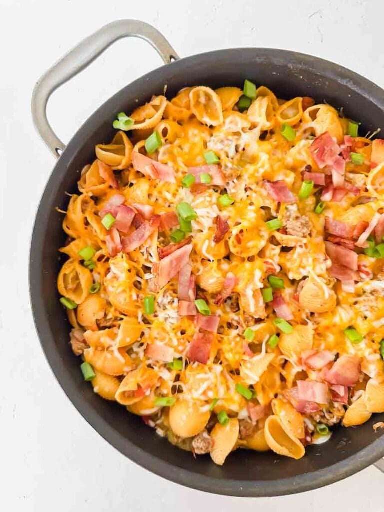 Cheesy pasta with bacon, green onions, and cheese in a large black skillet. This is bacon cheeseburger skillet.