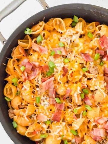 Cheesy pasta with bacon, green onions, and cheese in a large black skillet. This is bacon cheeseburger skillet.