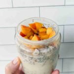 This is a picture of peach overnight oats. There is a glass jar filled with oats, chia seeds, and chopped peaches.