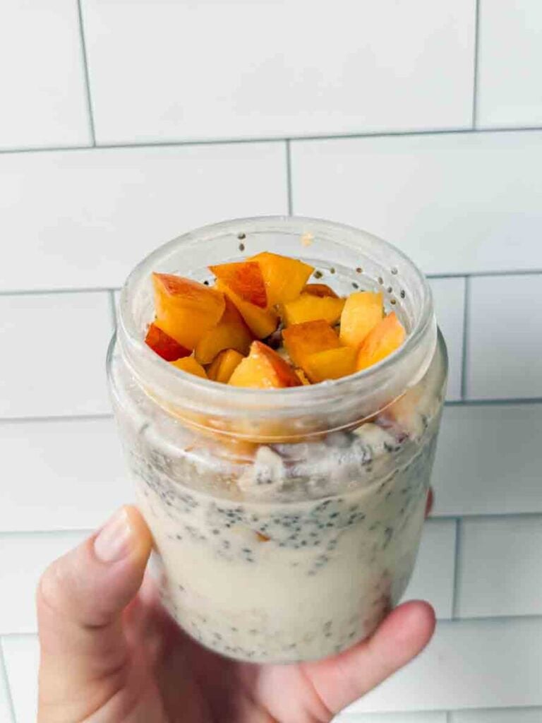 This is a picture of peach overnight oats. There is a glass jar filled with oats, chia seeds, and chopped peaches.