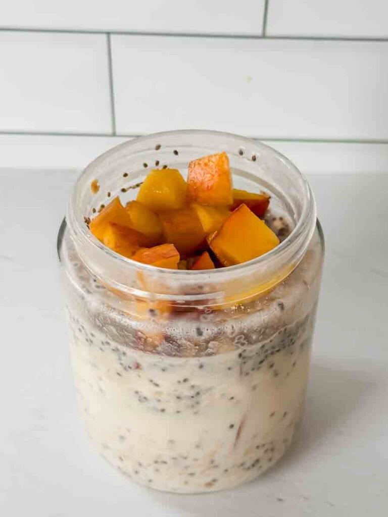 This is a picture of peach overnight oats. There is a glass jar filled with oats, chia seeds, and chopped peaches.