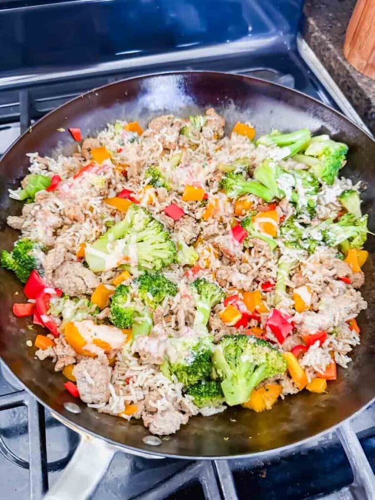 This is a skillet filled with bang bang turkey rice bowls. There's a skillet that has cooked turkey, broccoli, bell peppers, and rice.