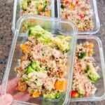 This is meal prep containers of bang bang turkey rice bowls. Each container has ground turkey, rice, broccoli, bell peppers, and a yummy sauce on top. A hand is holding up a container of the bang bang turkey bowl.