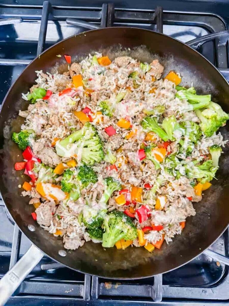 This is a skillet filled with bang bang turkey rice bowls. There's a skillet that has cooked turkey, broccoli, bell peppers, and rice.