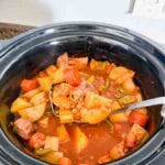 This is a crock pot filled with beef stew. There's beef chunks, potatoes, carrots, green beans, onions, and lentils.