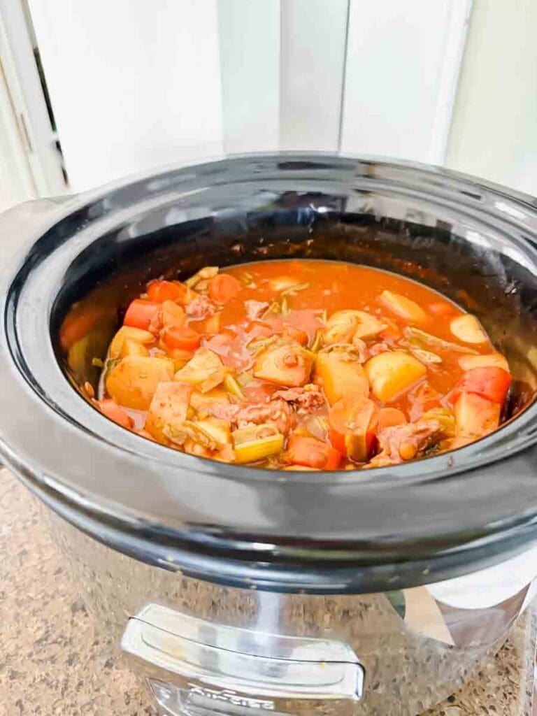 This is a crock pot filled with beef stew. There's beef chunks, potatoes, carrots, green beans, onions, and lentils.