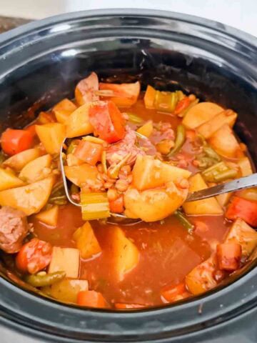This is a crock pot filled with beef stew. There's beef chunks, potatoes, carrots, green beans, onions, and lentils.