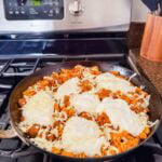 There is a large skillet of pumpkin pasta topped with dollops of high-protein cheese.