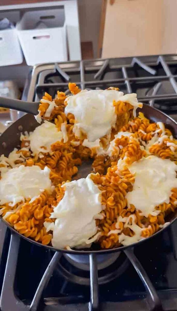 There is a large skillet of pumpkin pasta topped with dollops of high-protein cheese.